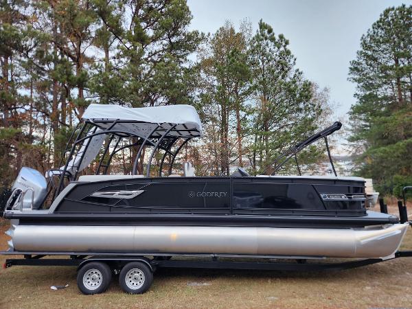 Godfrey AquaPatio Sundeck 275 SDC 2025 Godfrey AquaPatio Sundeck 275 SDC pontoon boat on trailer, surrounded by trees.