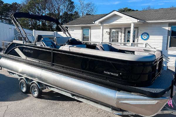 Godfrey Sweetwater 24' Drop Table Lounge Tritoon - 2486 DT 2025 Godfrey Sweetwater 24' Drop Table Lounge Tritoon on trailer, parked outside a building.