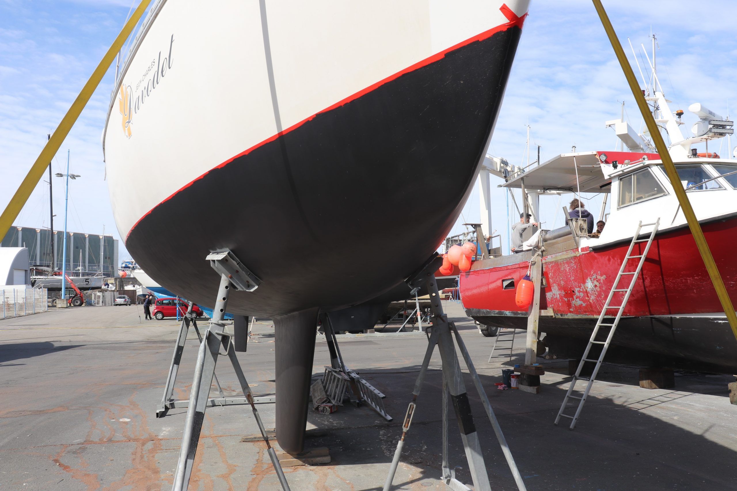 Un bateau est levé pour l'application de ruban de masquage au niveau de la flottaison afin de conserver une ligne droite et nette.