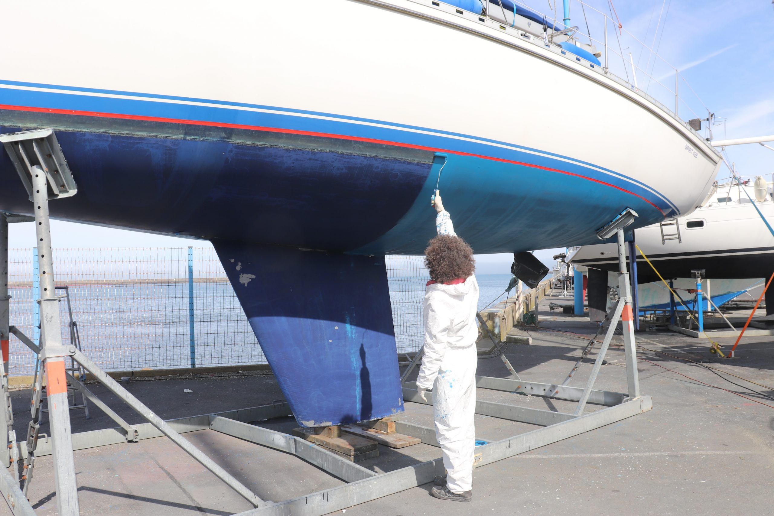 Un bateau est levé pour l'application de peinture antifouling à l'aide d'un petit rouleau.