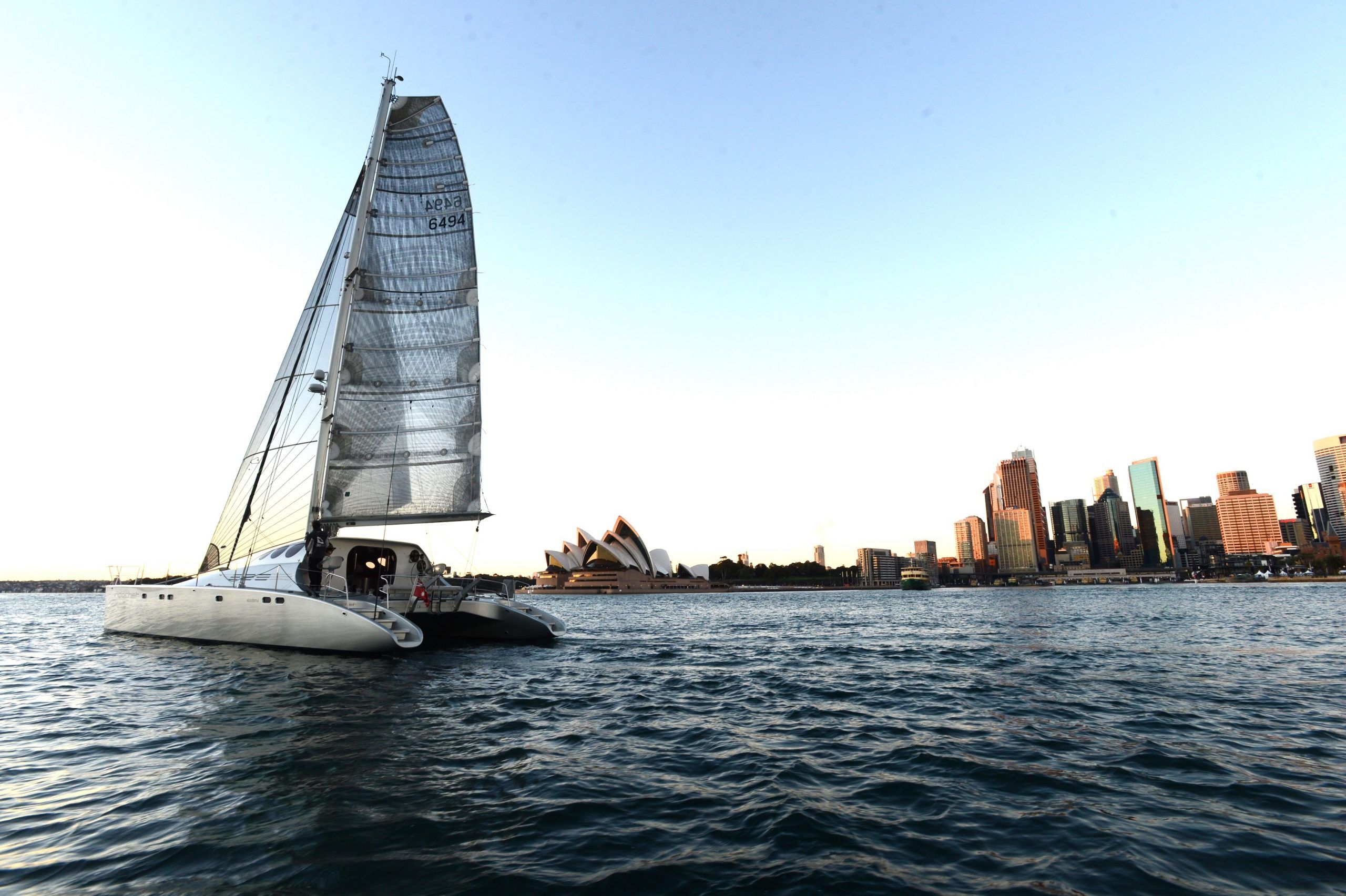 Catamaran Ricochet sails by Sydney harbour at sunset