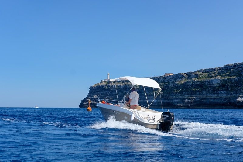 Een witte motorboot met een zonnescherm op de oceaan met rotsachtig land op de achtergrond.
